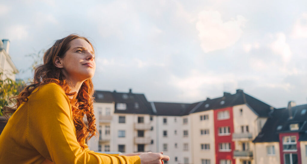 Frau vor Häuserblock schaut in den Himmel. Joyce Meyer