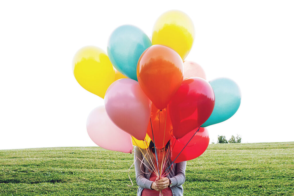 Frau hält mehrere bunte Luftballons in der Hand. Joyce Meyer